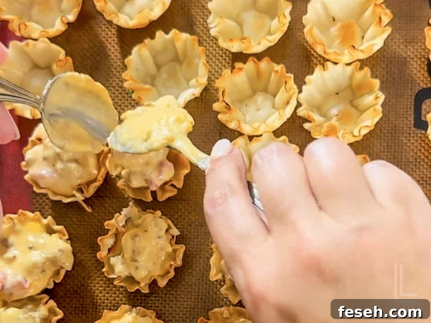 spooning the melted cheese mixture into phyllo cups on a baking sheet.
