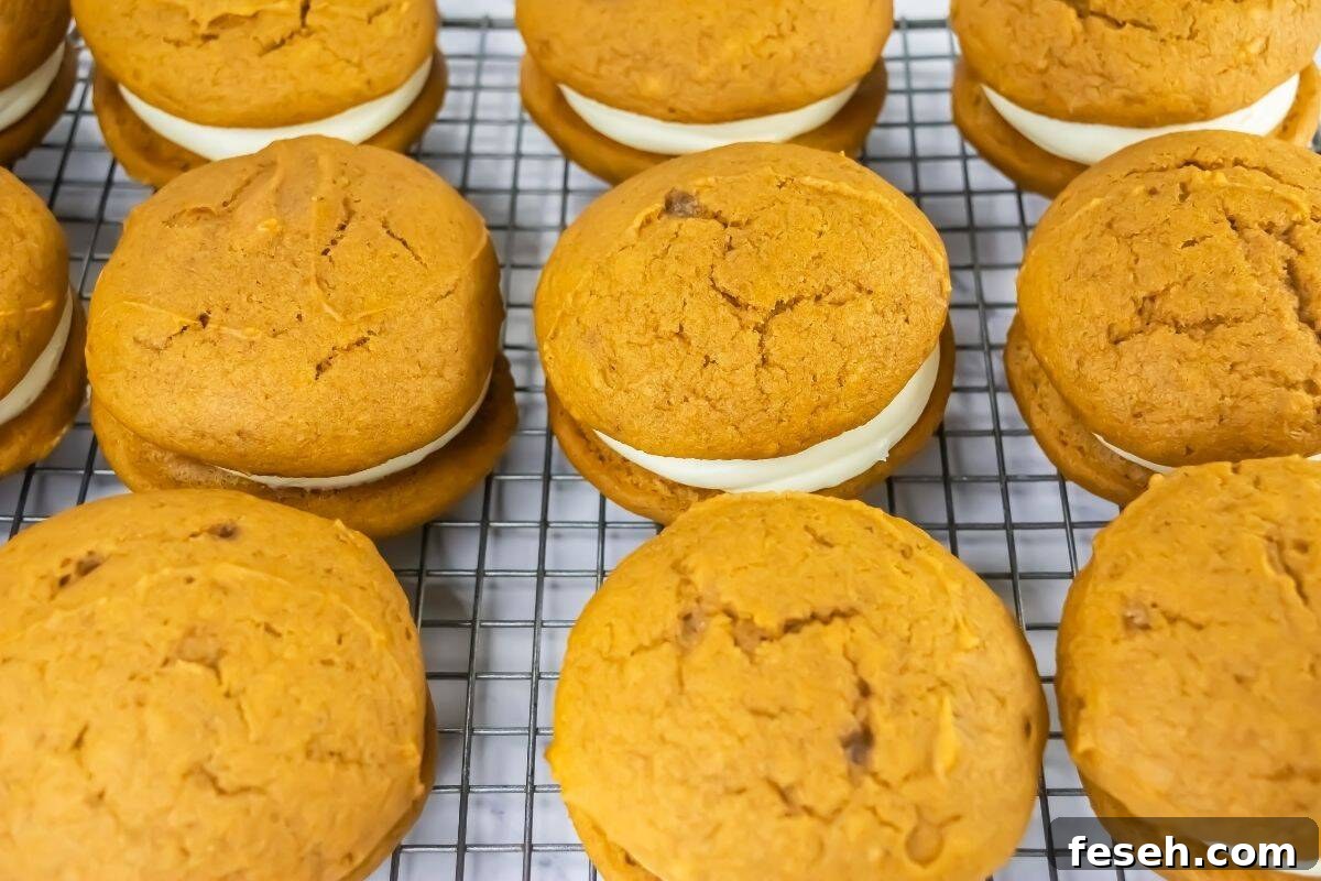 Pumpkin whoopie pies with cream filling are arranged in rows on a wire cooling rack.