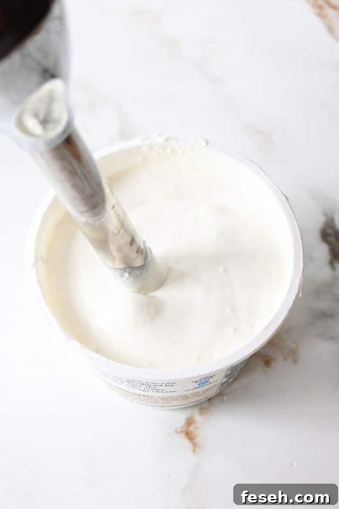 Cottage cheese being blended in a container with an immersion blender.