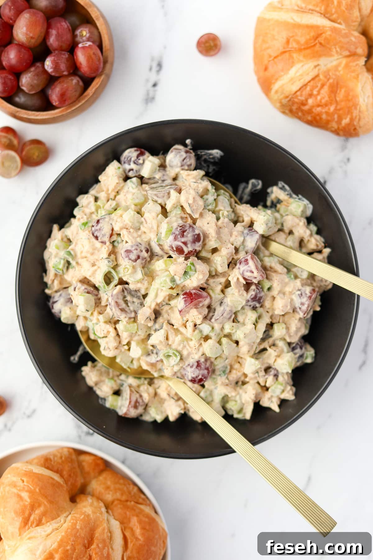 A bowl of chicken salad being tossed with serving spoons.