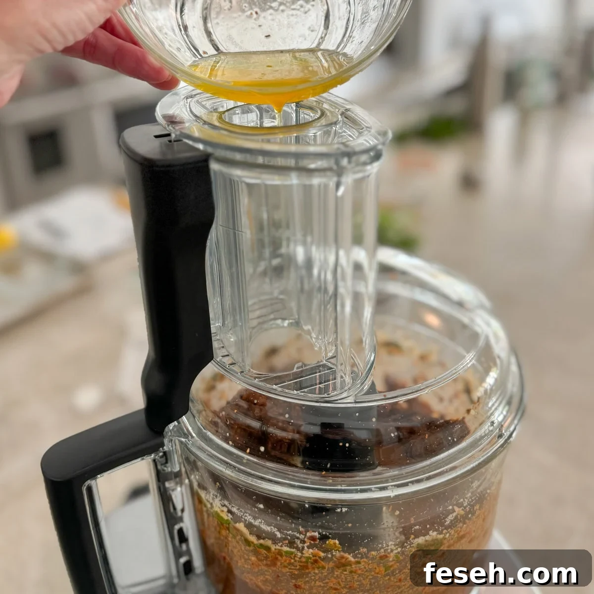 Drizzling olive oil into a food processor through the feed tube.