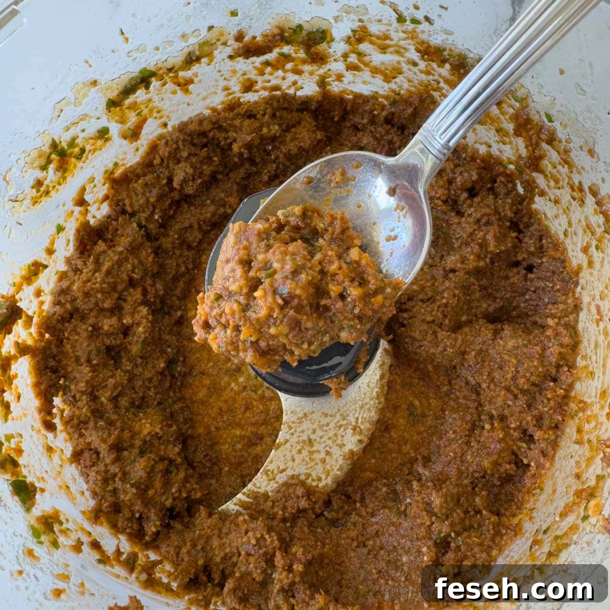 Rich reddish brown tomato pesto on a spoon.