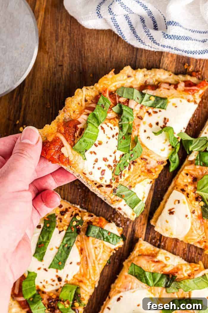 hand reaching out to grab slice of keto chicken crust pizza off cutting board