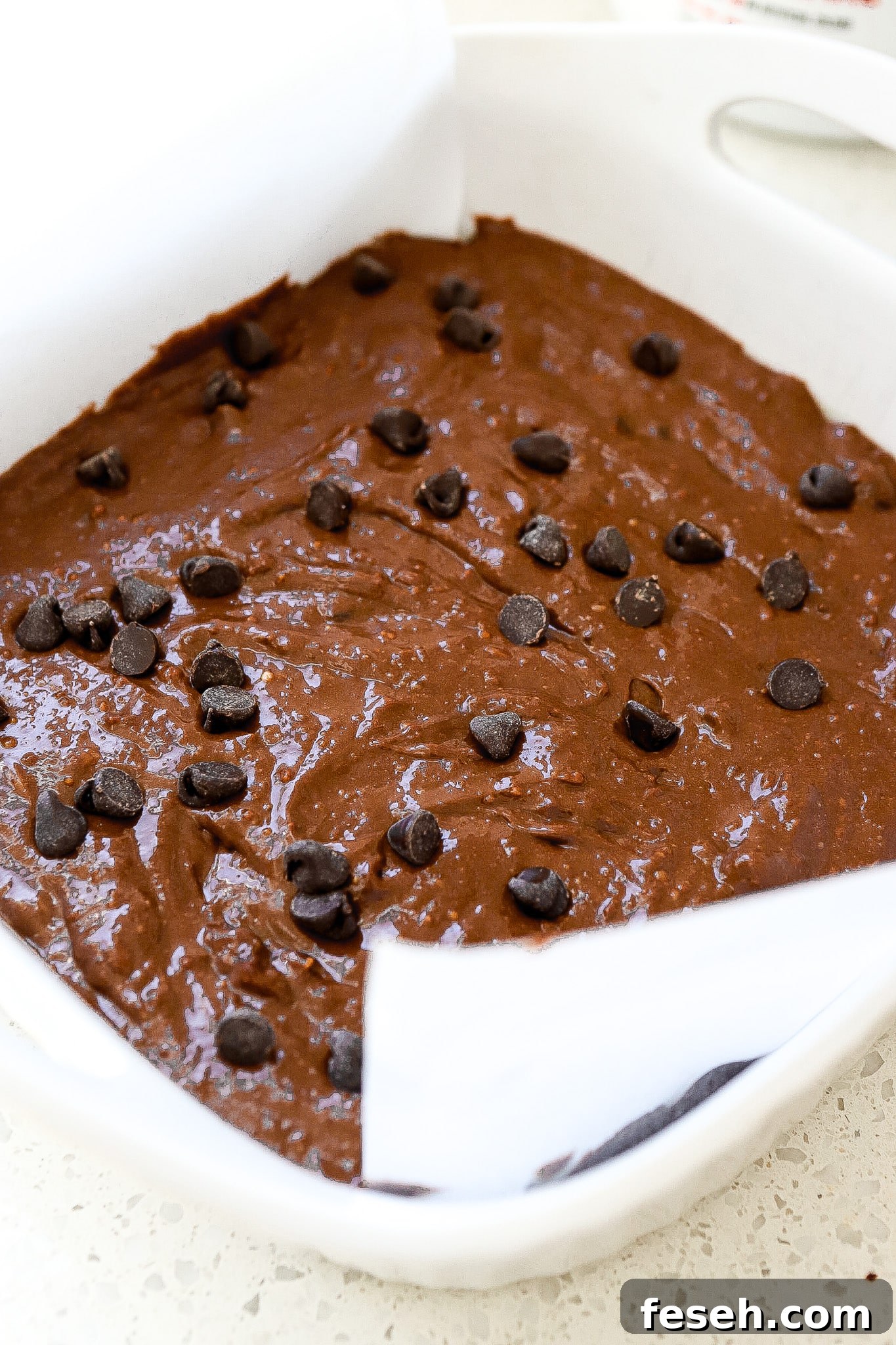 Side view of protein chocolate brownie batter in white baking dish with parchment paper.