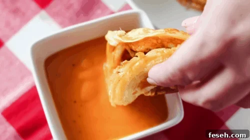 Dipping keto chaffle with onion ring in sauce.