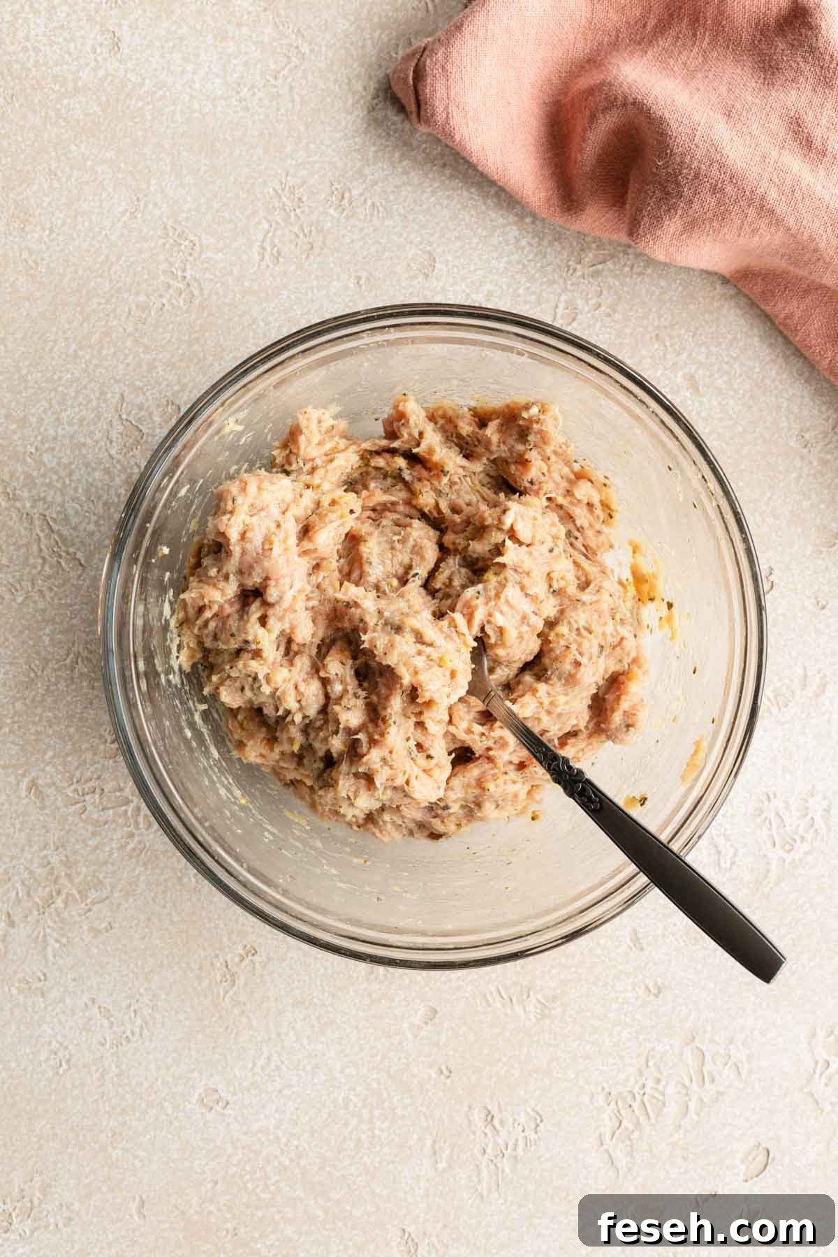 Burger ingredients mixed together in a glass bowl with a fork.
