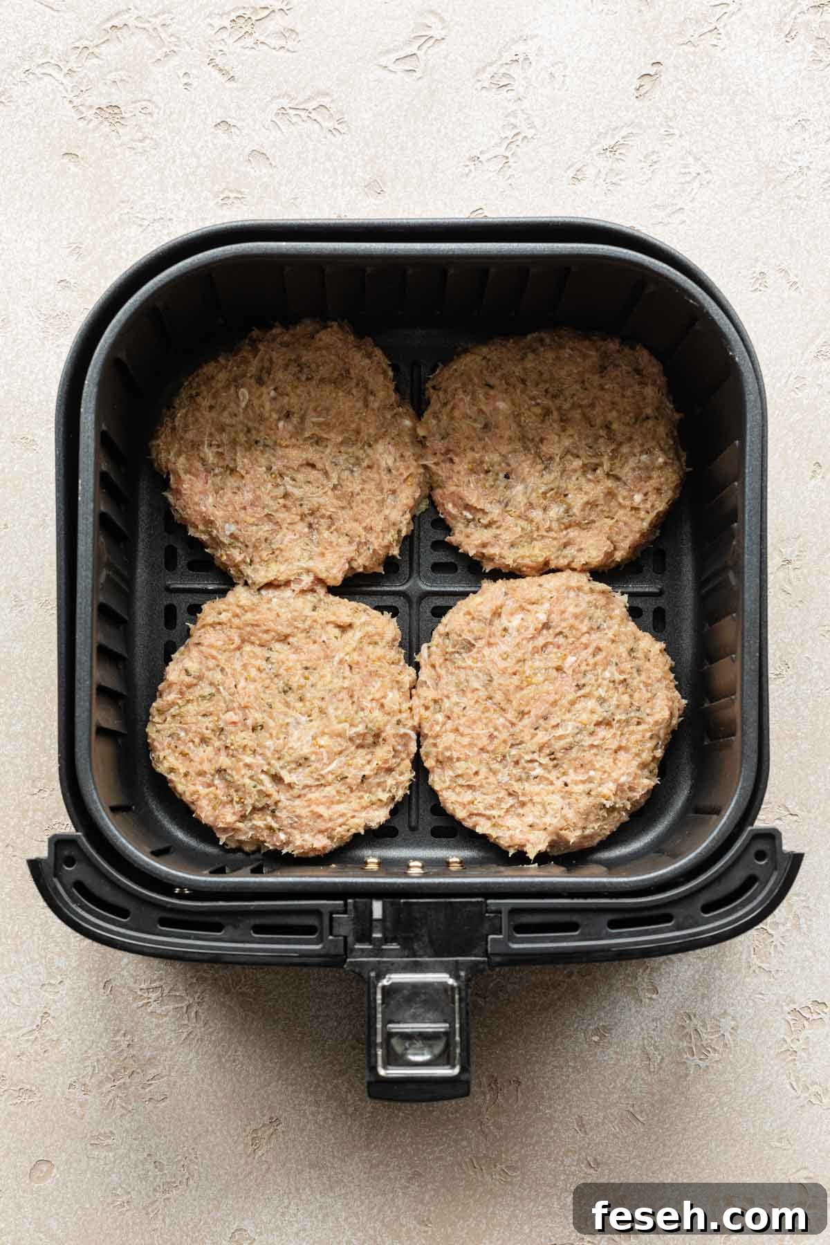 Four turkey burger patties in an air fryer basket.
