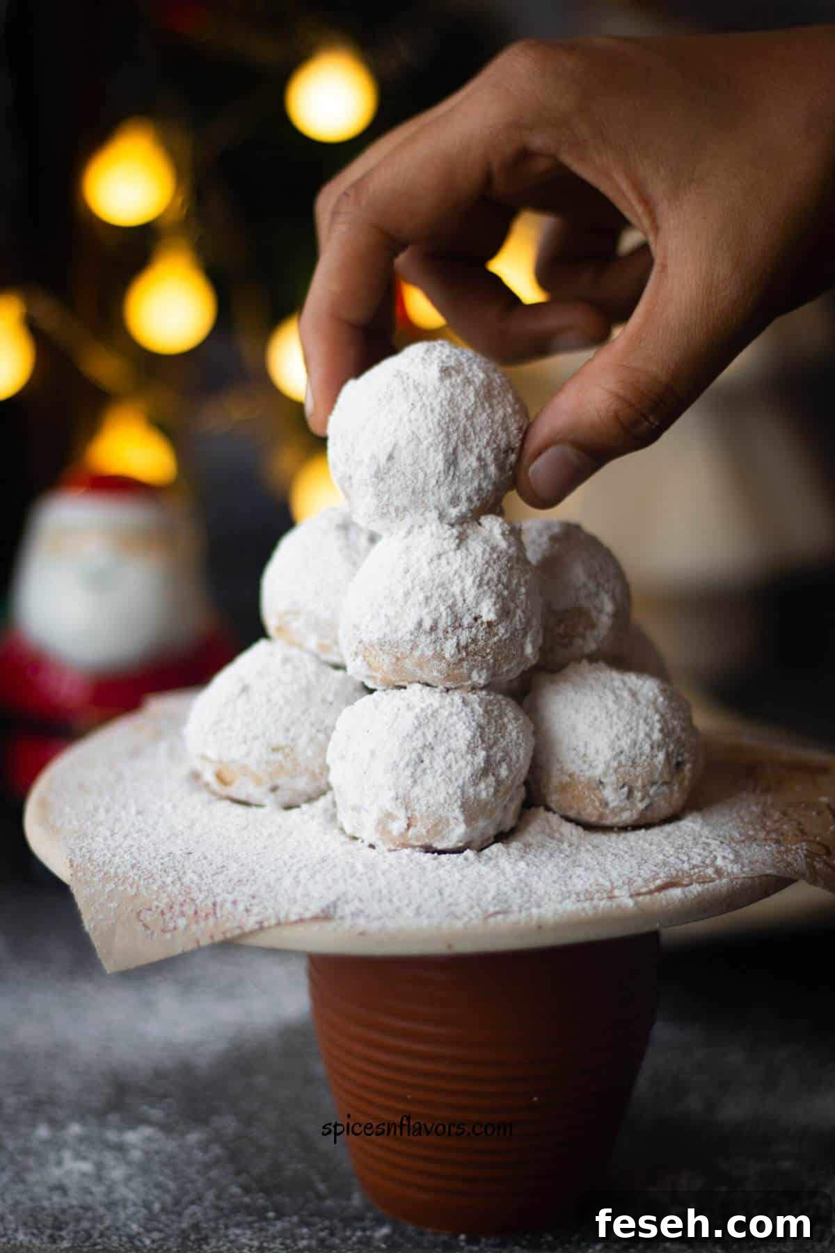 a piece of snowball cookies lifted using fingers that was stacked on a pyramid of other snowball cookies