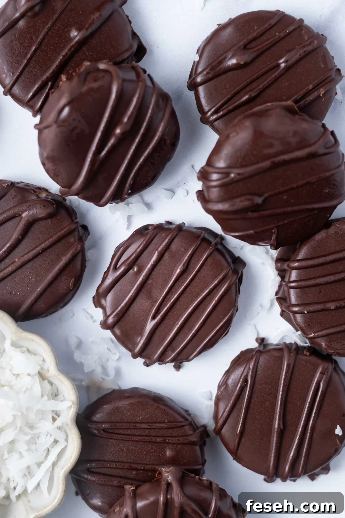 chocolate dipped coconut patties on a marble counter with a bowl of coconut