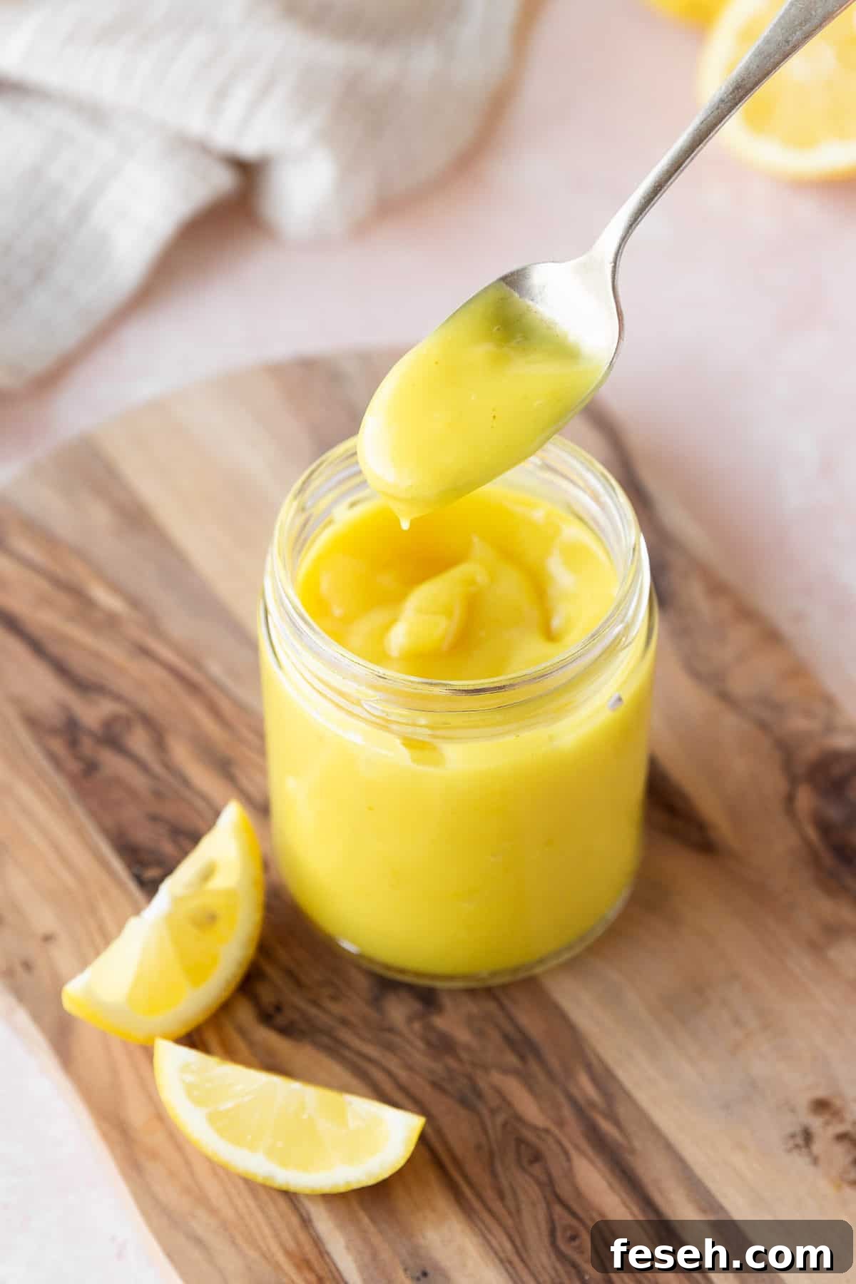 45 degree angle shot of a spoonful of vegan lemon curd above the mason jar to show the thick consistency.