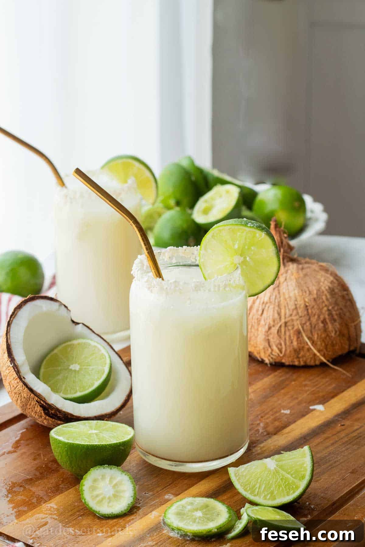 Glass of lime in the coconut drink with straw and lime slice and pitcher of limeade.