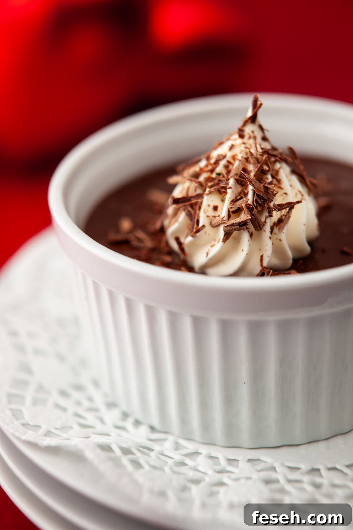 White ramekin of dark chocolate pudding, called pots de creme, on a white plate with lacey paper.