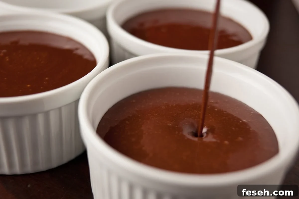 Pouring liquid batter for chocolate pots de creme into white ramekins to set for dessert.