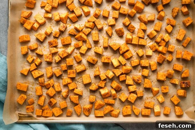 Chopped and seasoned sweet potatoes, uncooked, on a sheet pan.