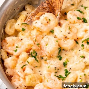 a wooden spoon resting in a silver skillet filled with creamy gnocchi shrimp scampi