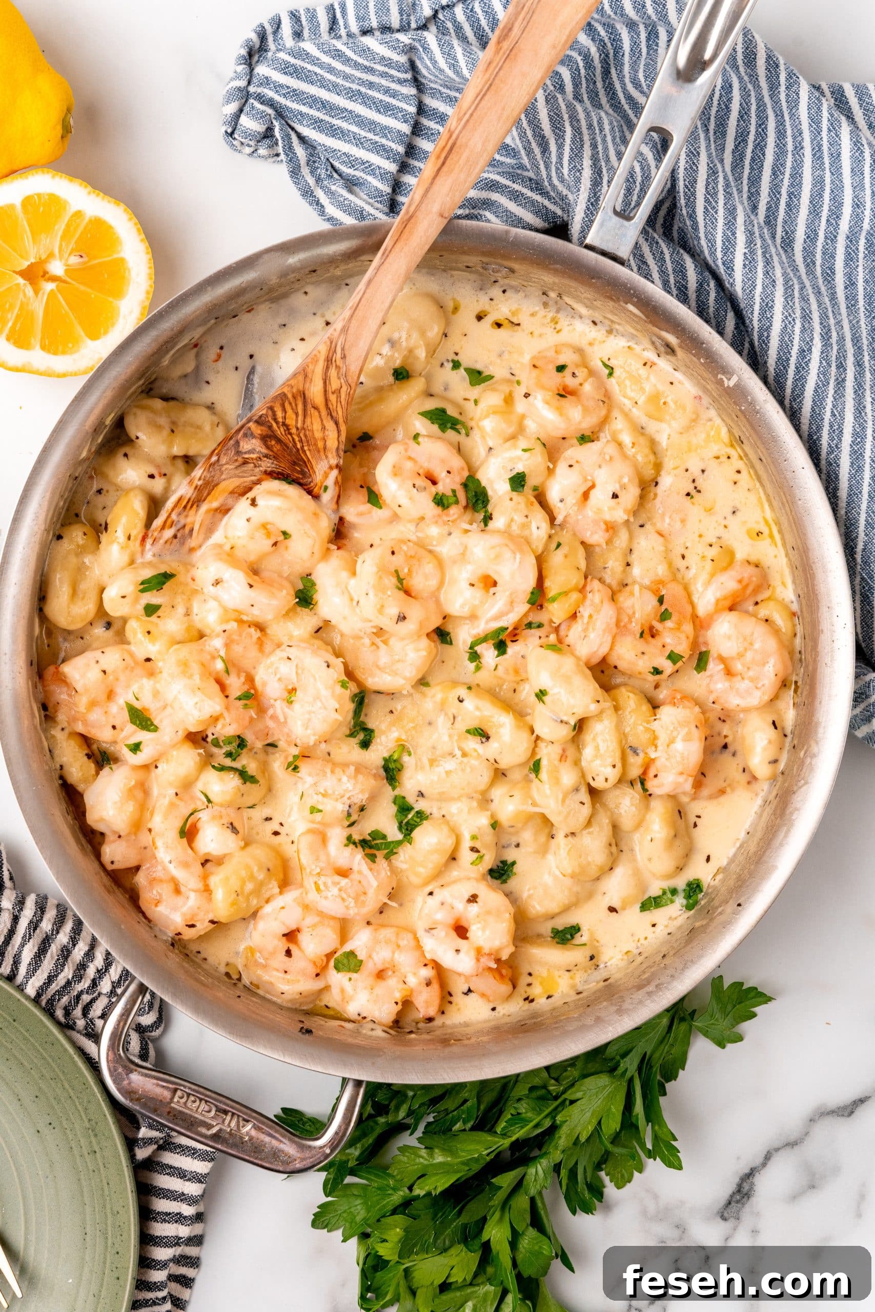 a wooden spoon resting in a silver skillet filled with creamy gnocchi shrimp scampi