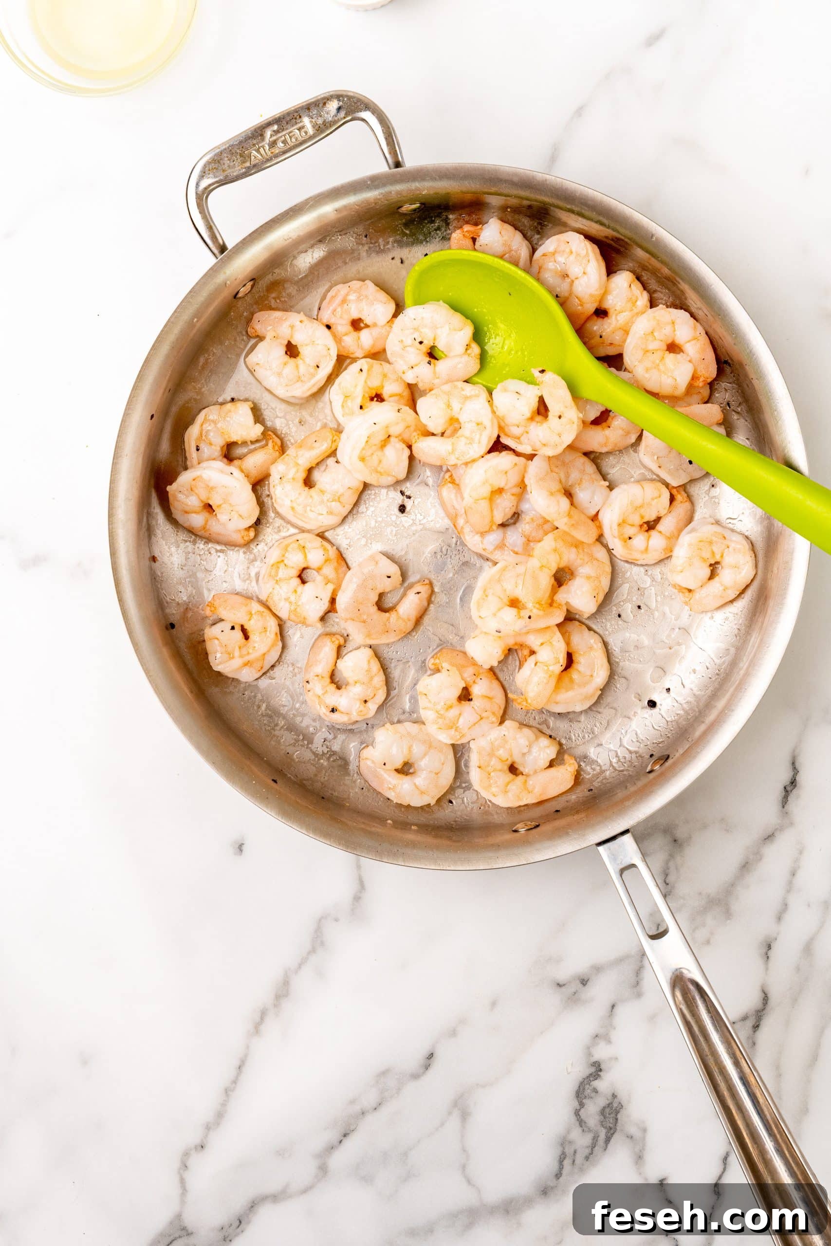 sauteed shrimp in a large silver skillet with a green spoon resting on the side