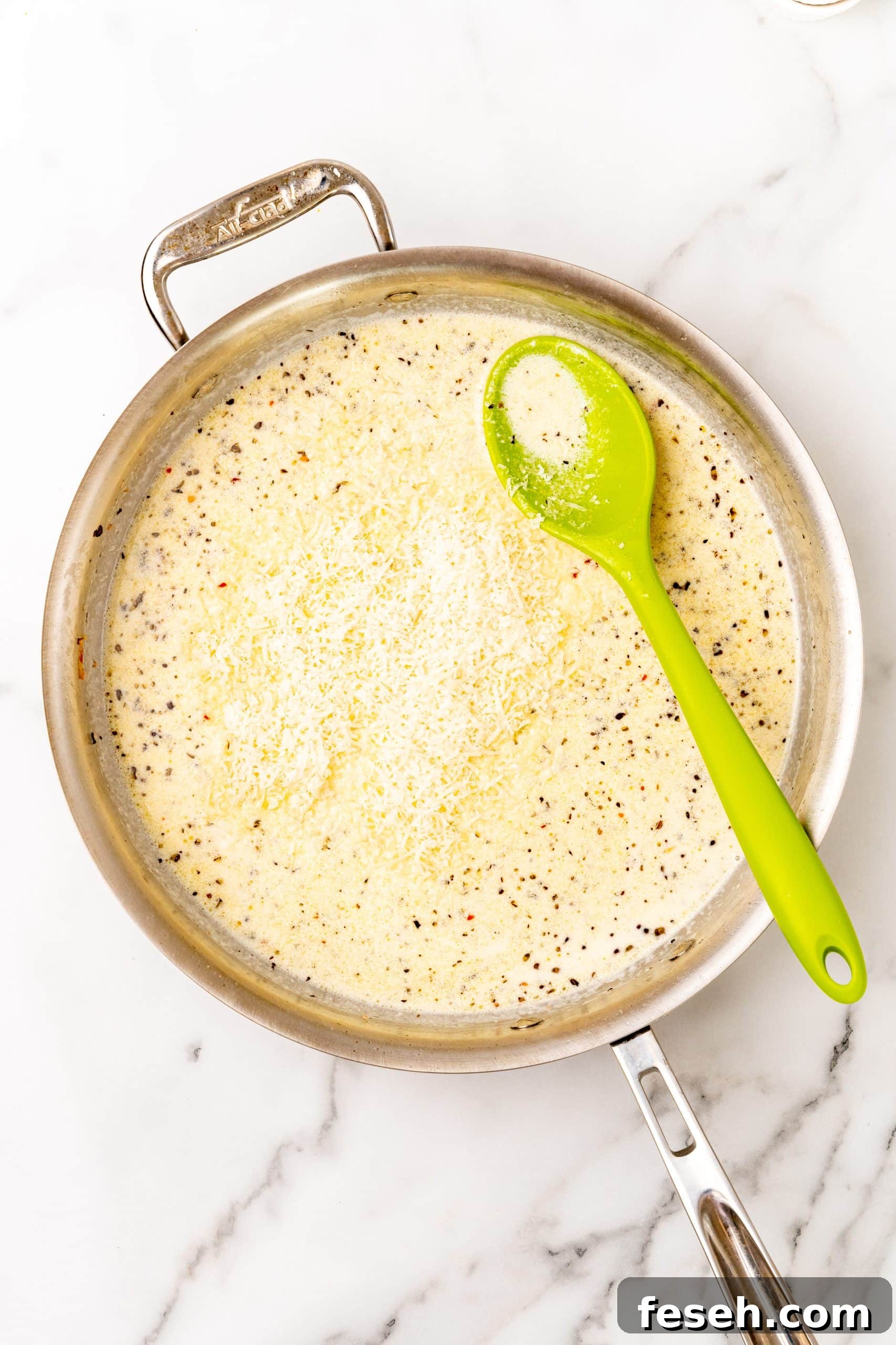 parmesan cheese added to a large silver skillet filled with a creamy garlic butter scampi sauce