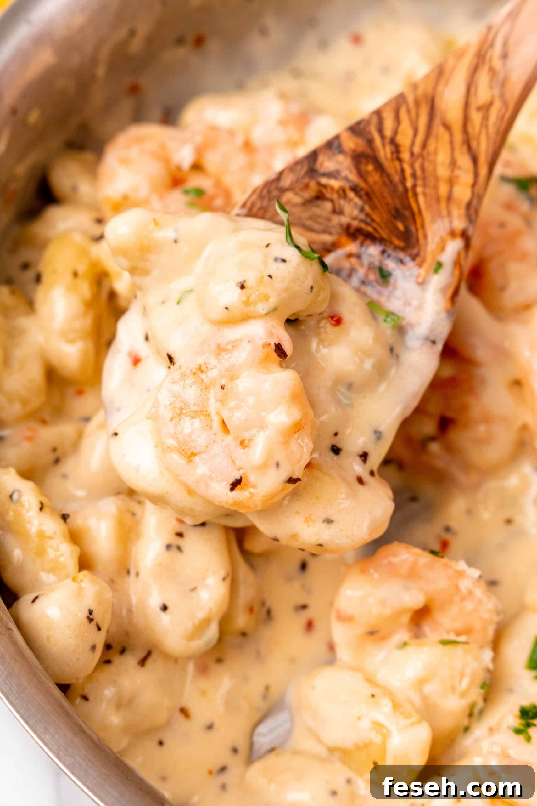 a wooden spoon holding up a scoop of creamy shrimp scampi gnocchi