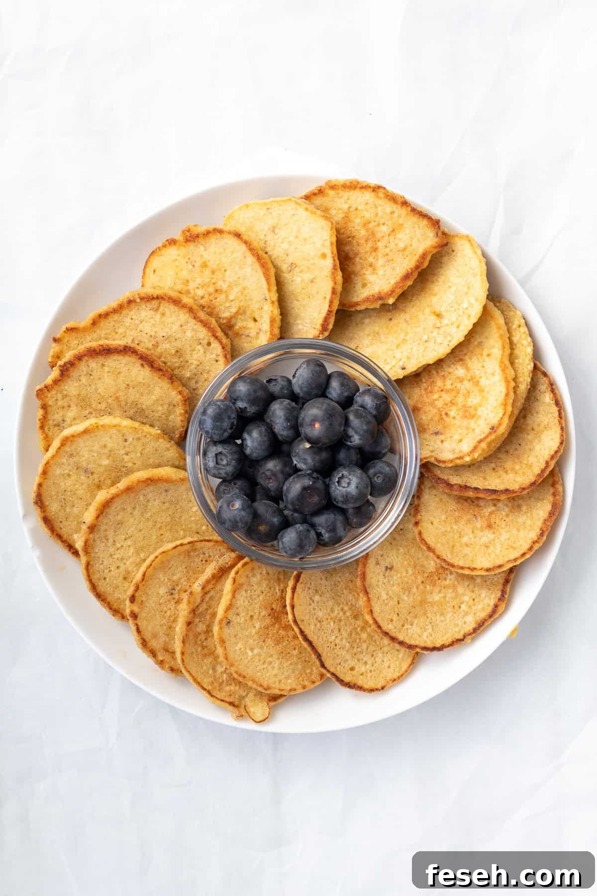 pancakes on a round serving platter with a bowl of blueberres in the middles