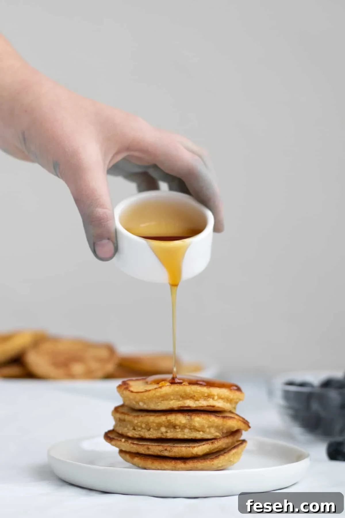 syrup being poured over pancakes from a small white bowl