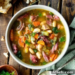a photo of a large bowl of ham and bean soup with a large chunk of crusty bread next to it and a spoon