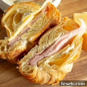 a ham and cheese sandwich on a flaky croissant that has been sliced in half so you can see the inside of each half
