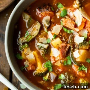 a photo of a bowl of hearty ham and vegetable soup loaded with potatoes, carrots, tomatoes, mushrooms and topped with chopped parsley