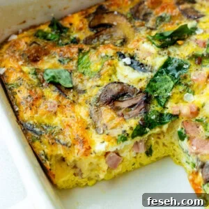 a baking dish of a baked egg, spinach and sauteed mushroom casserole with a serving missing so you can see the cross-section of the casserole