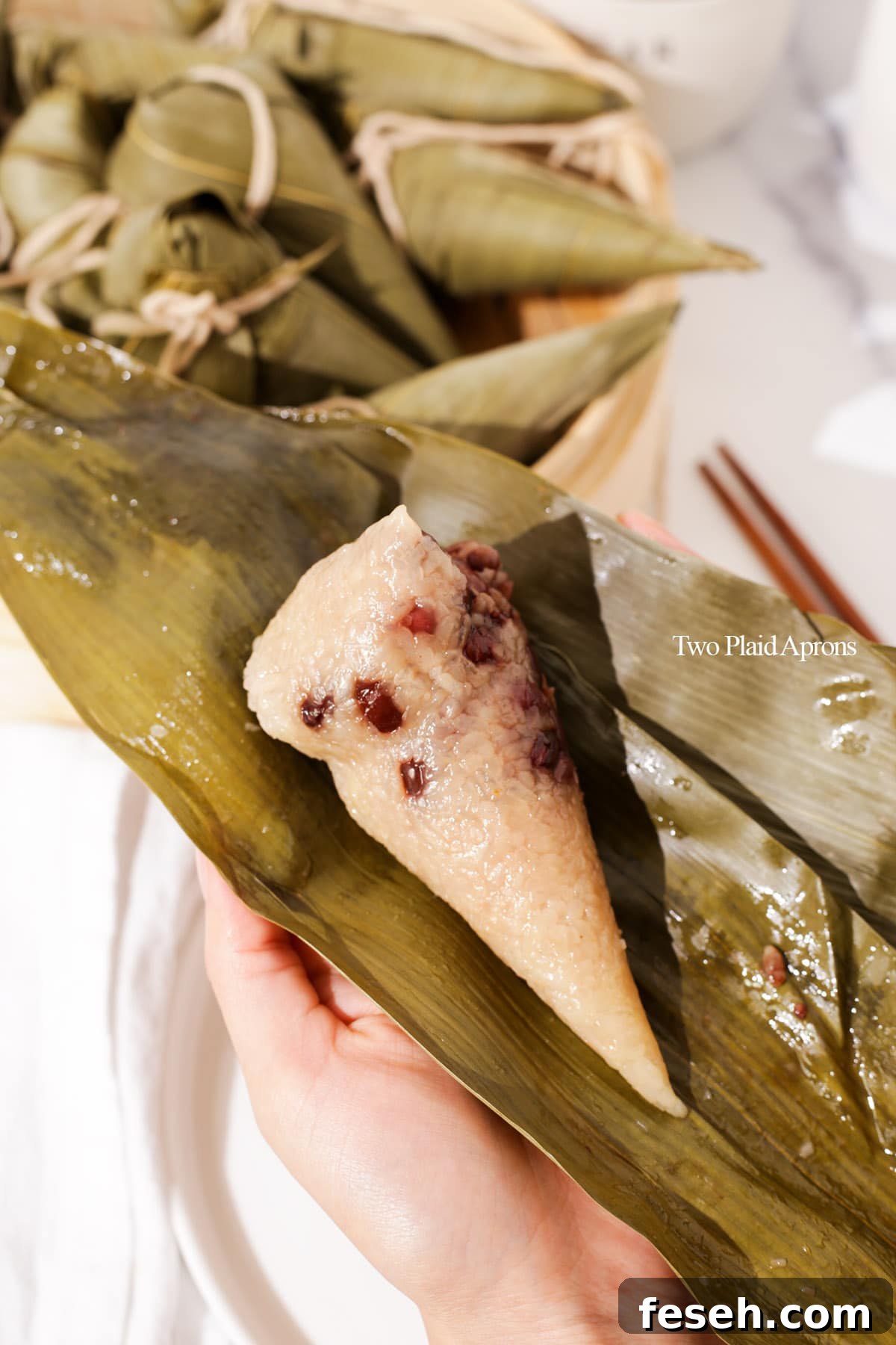 Holding an unwrapped red bean sticky rice dumpling with bamboo leaves.