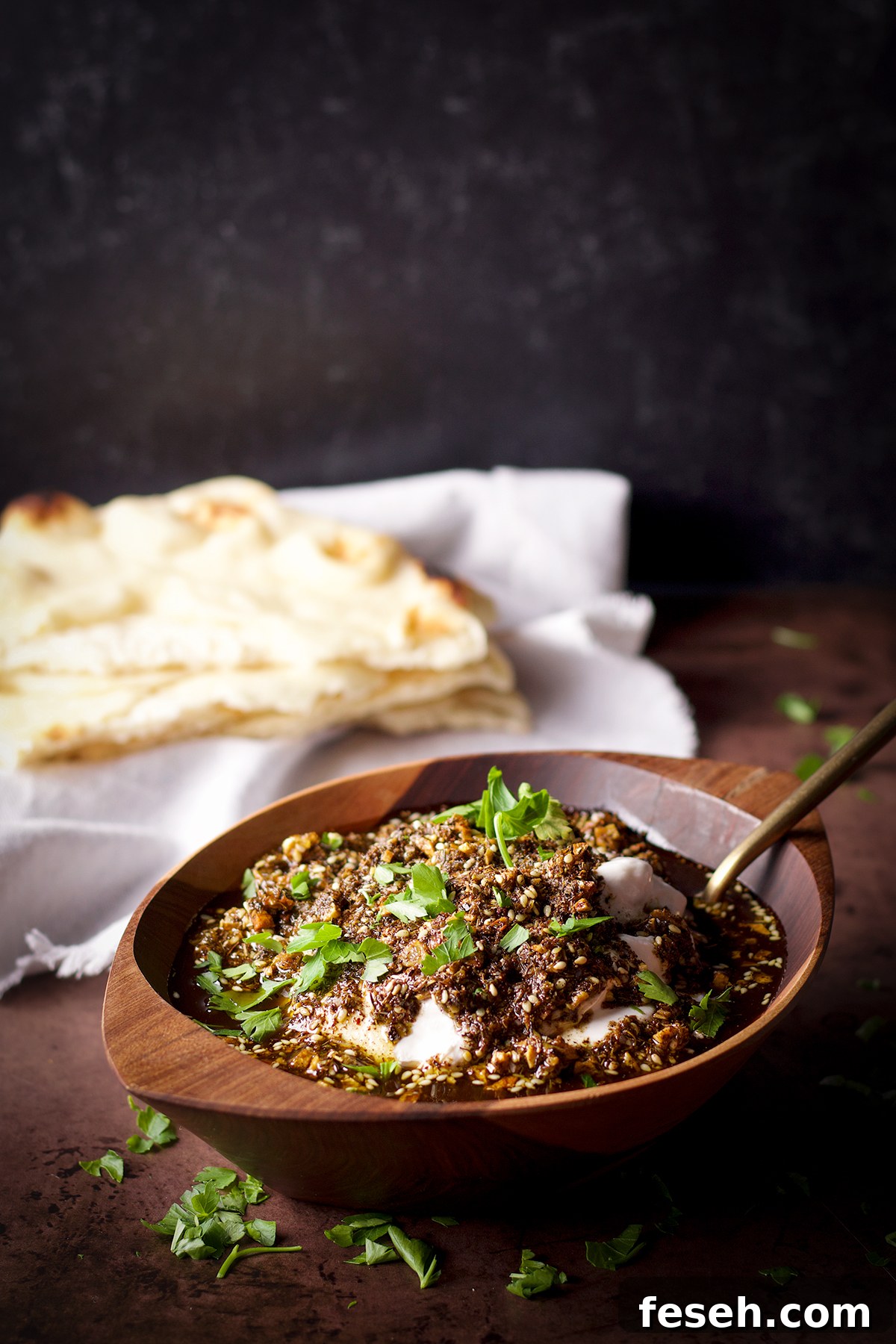 A wood bowl filled with za'atar labneh sitting next to a stack of buttered naan.