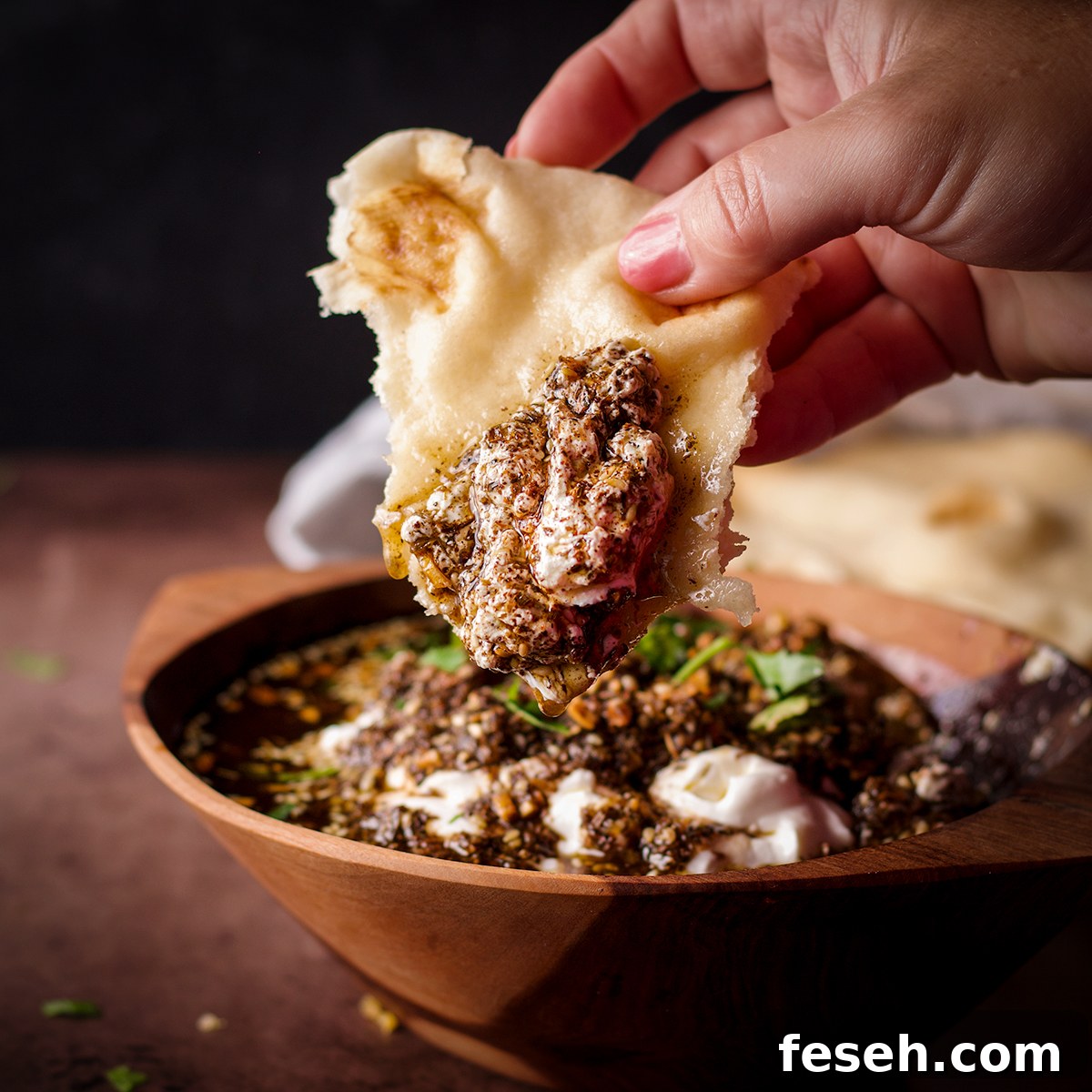 Someone dipping a piece of naan into a bowl filled with za'atar labneh.