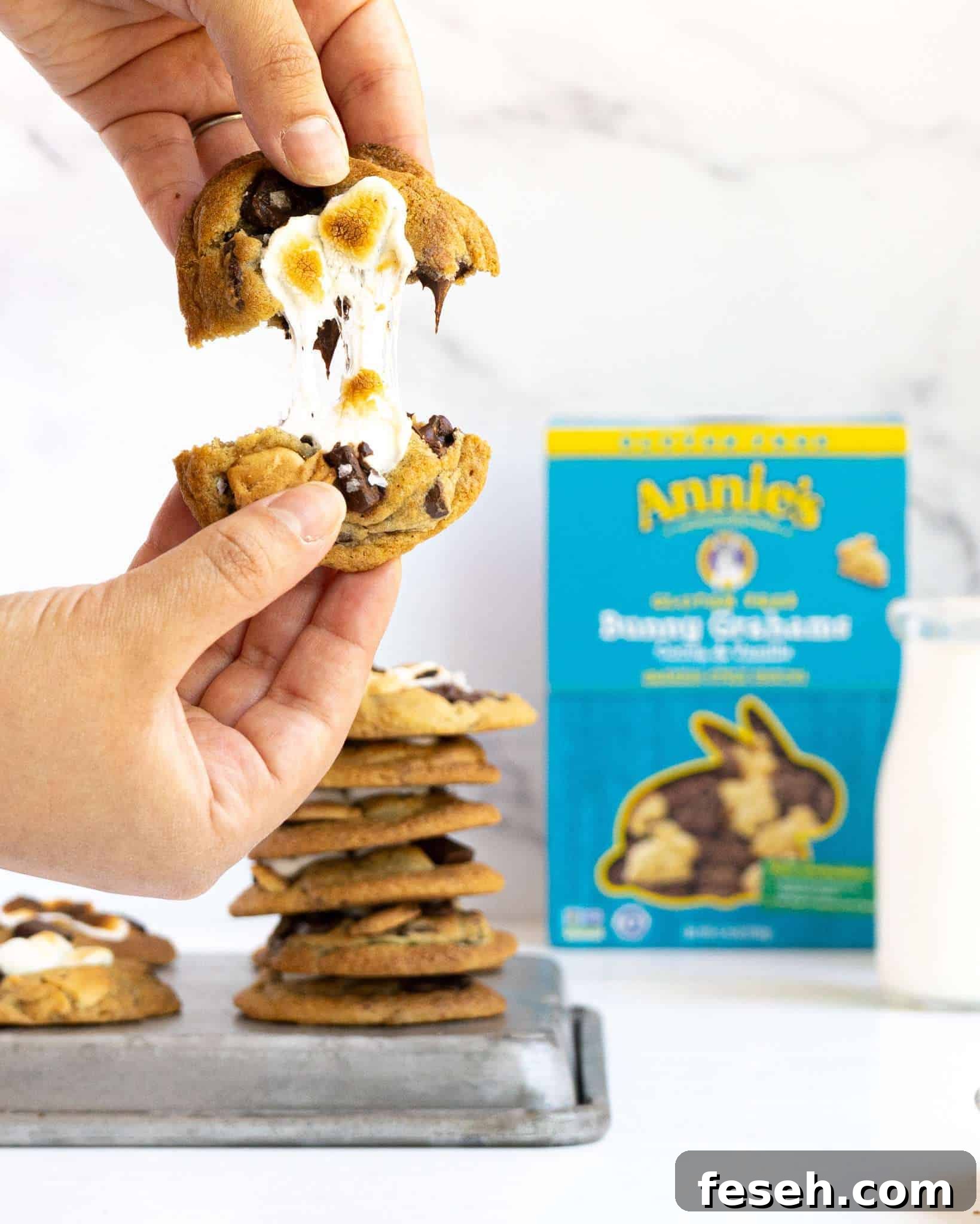 Two hands pulling apart a melty marshmallow s'mores cookie.