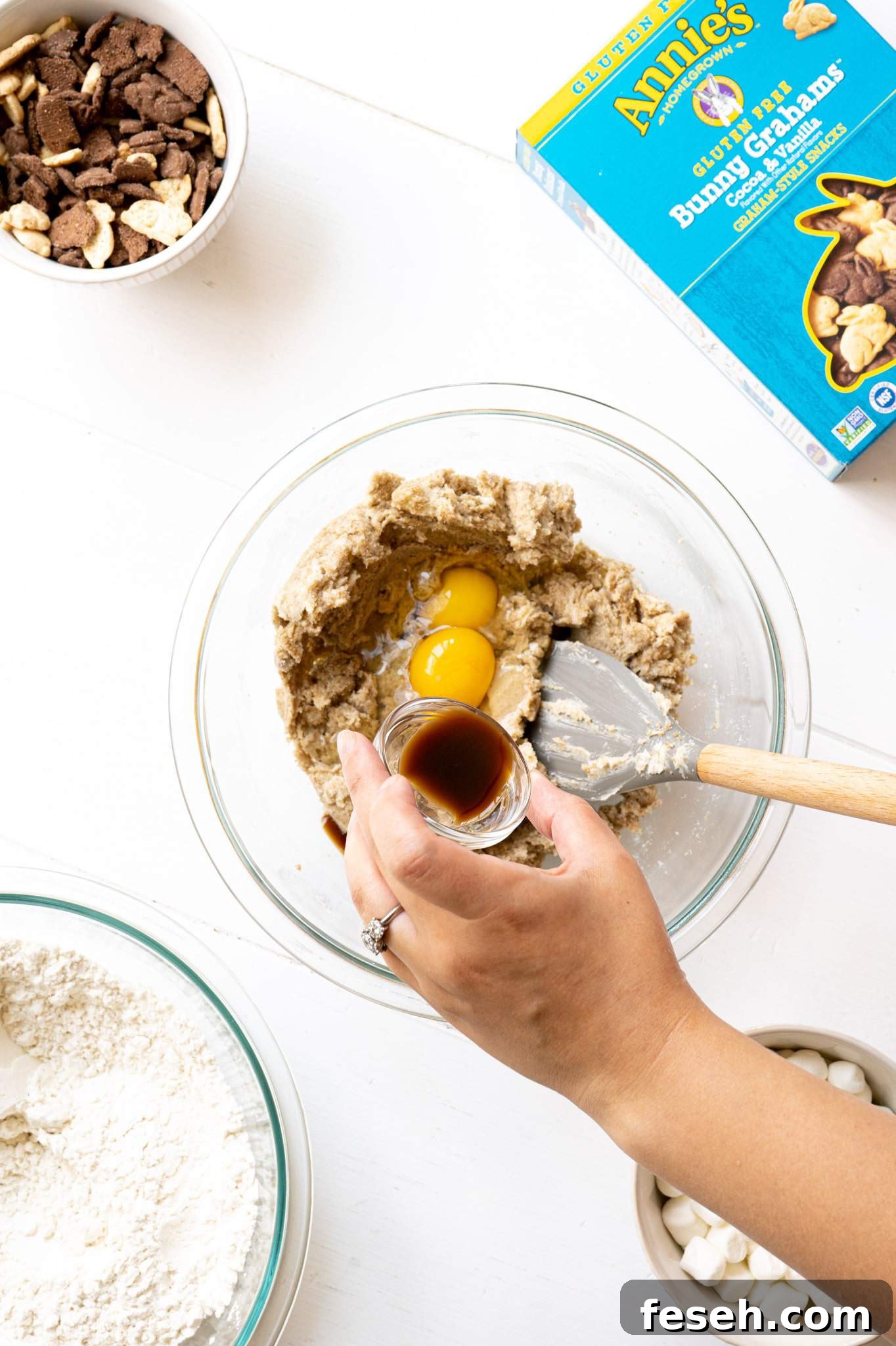 A hand pouring vanilla into cookie dough with eggs.