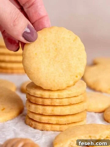 A hand grabbing an orange shortbread cookie from a stack.