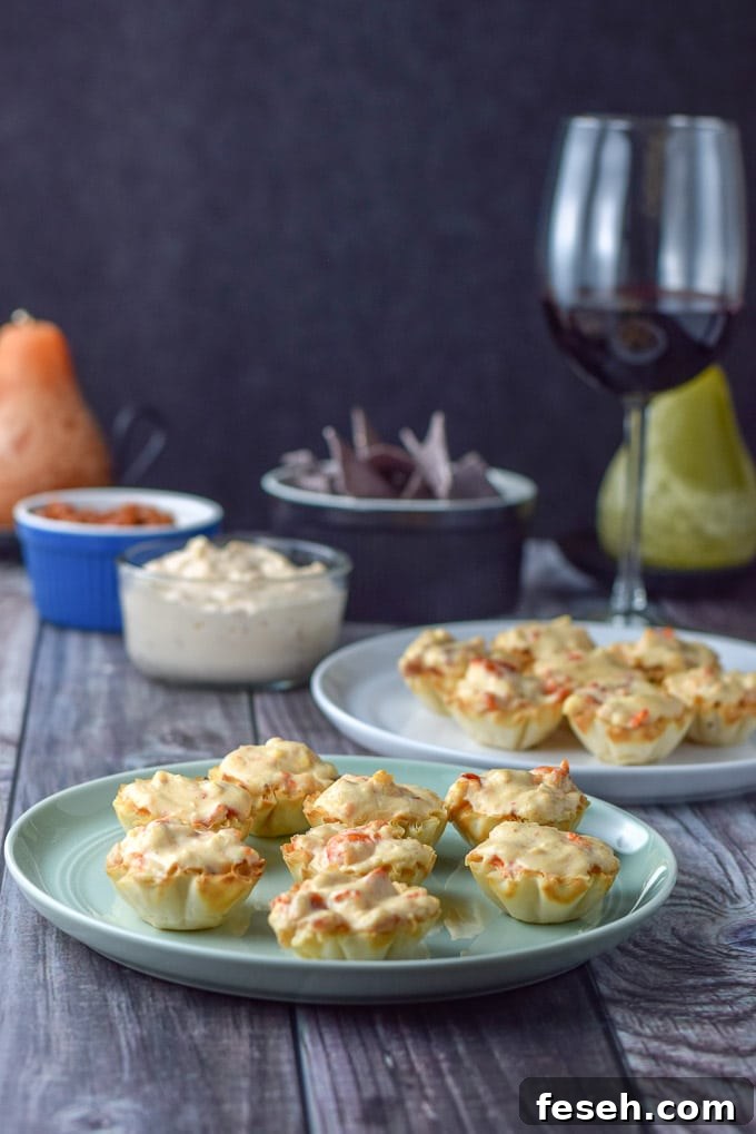 A green plate with phyllo cups filled with the lobster and cream cheese with more dip in the back and a glass of wine