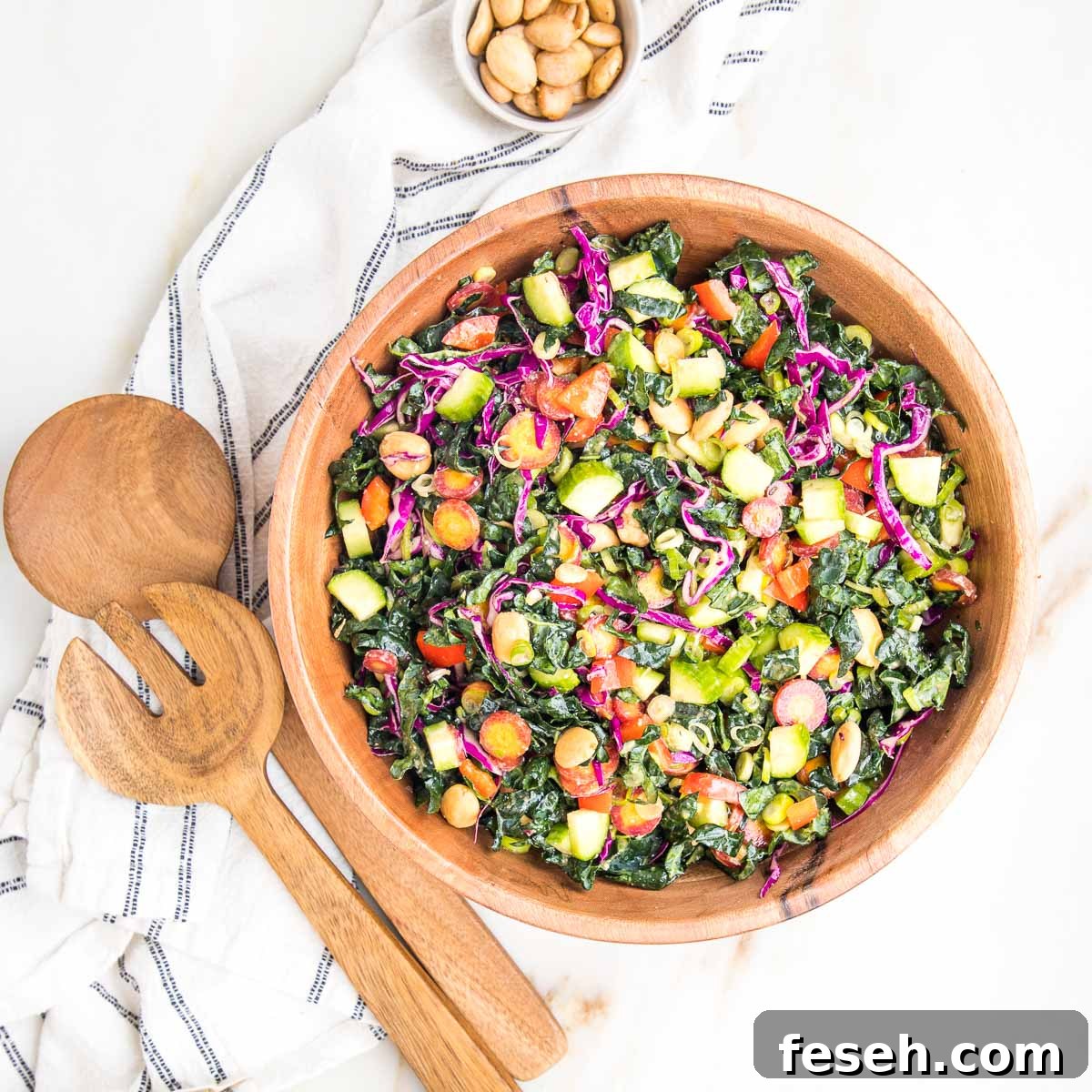 Colorful chopped salad in a wooden bowl with wooden salad tossers on the side and a bowl of marcona almonds. 