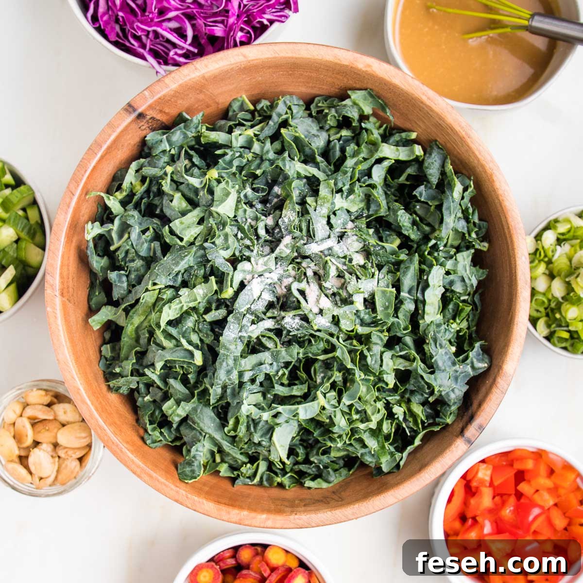 Thinly sliced tuscan kale with small bowls of colorful ingredients all around the bowl of kale.