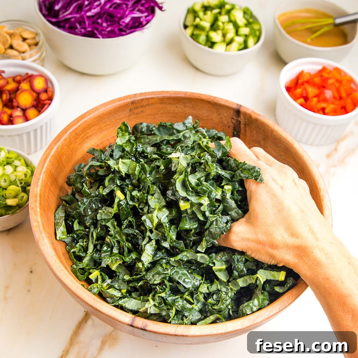 Wooden bowl, filled with chopped tuscan kale, being massaged by hand.