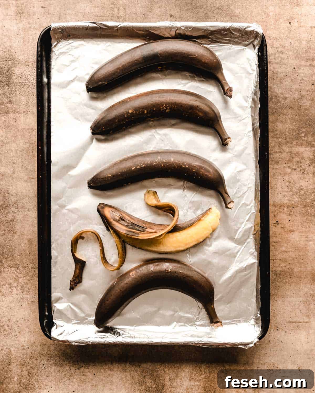 Brown bananas sitting on a foil covered baking sheet with one bananas peeled open.