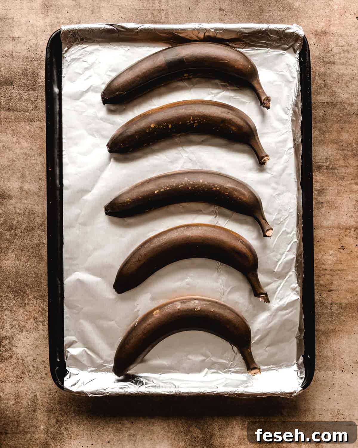 Brown bananas sitting on a baking sheet that's covered by goil