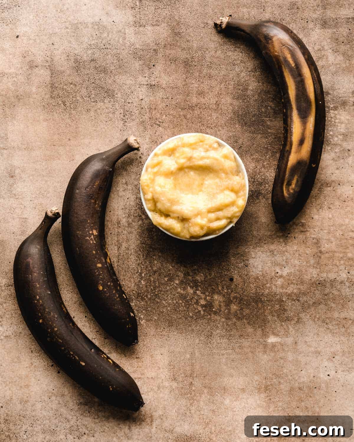 Brown bananas laying around a bowl of mashed bananas.