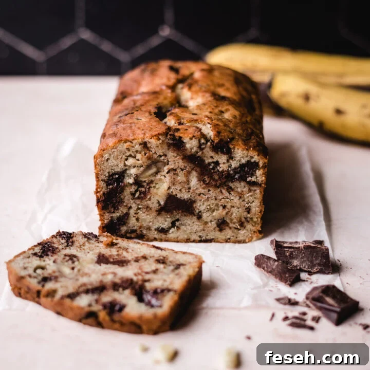 Banana bread sliced with chocolate chunks on the side and bananas behind.