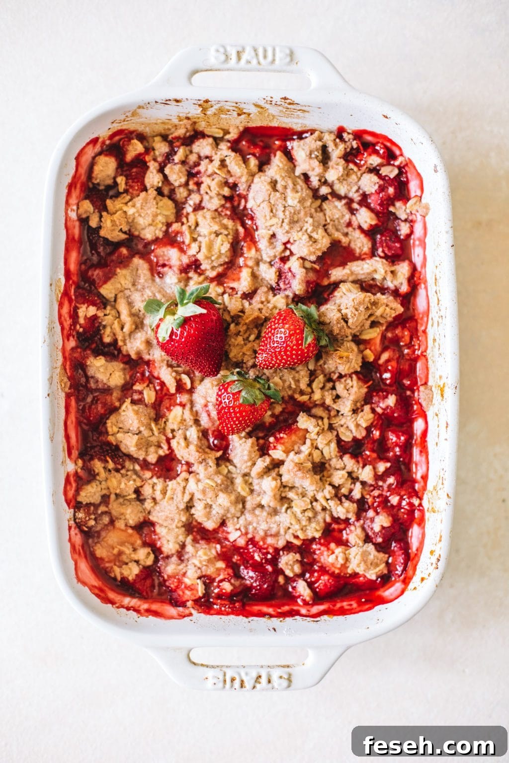 summer fruit crisp in white casserole dish topped with fresh strawberries