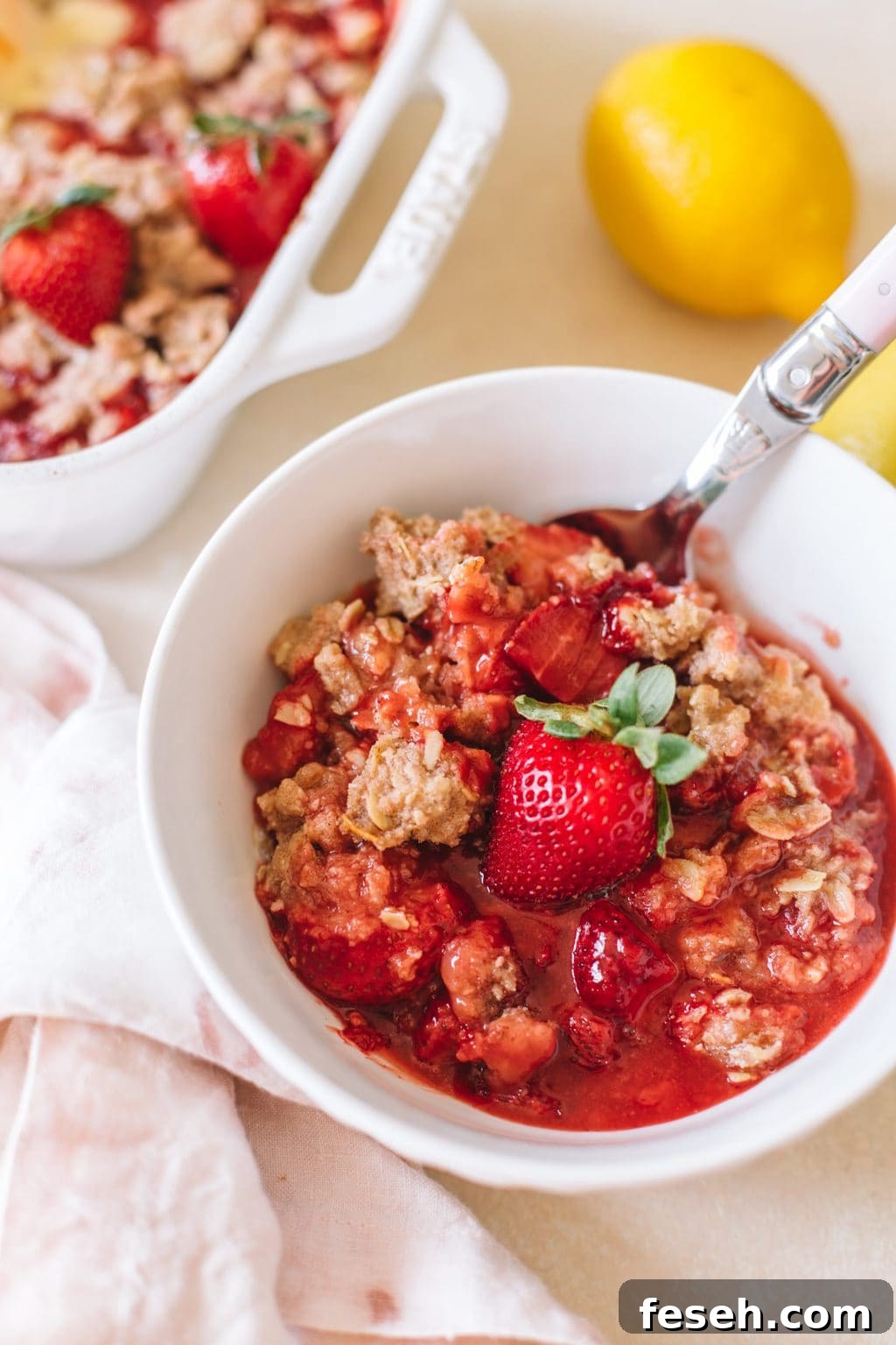 easy strawberry crumble recipe in white bowl with spoon and lemon on the side