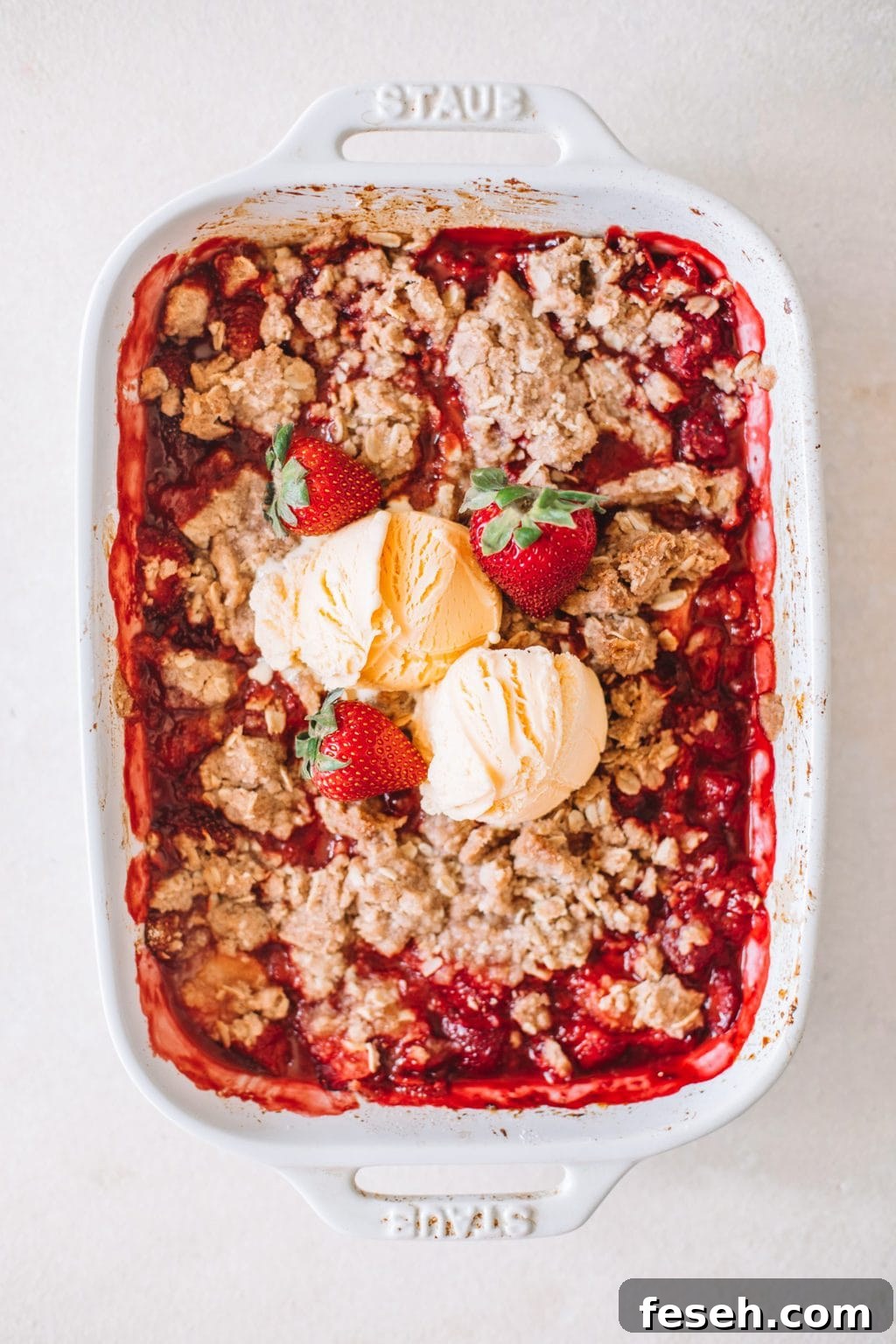 fresh strawberry crumble recipe in white casserole dish topped with vanilla ice cream