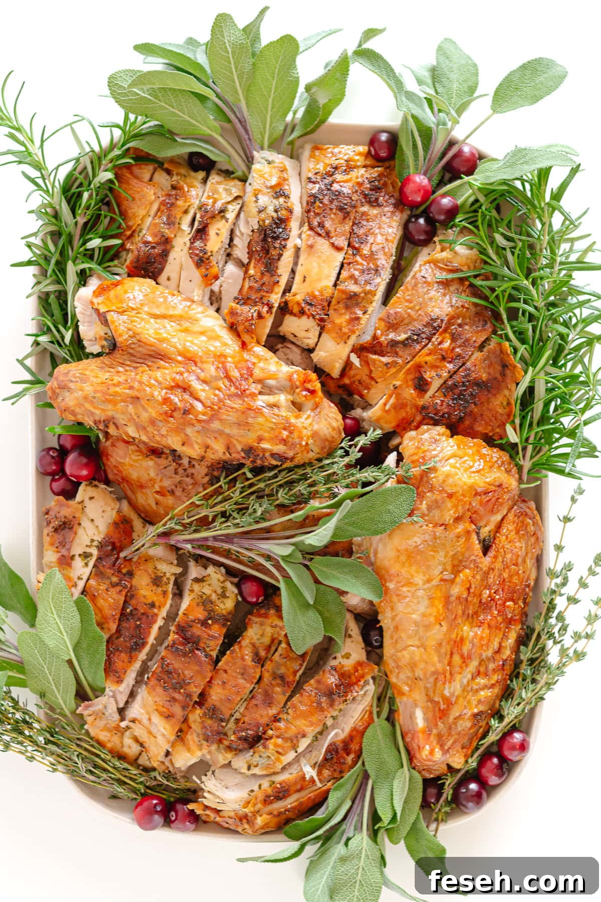Platter of carved roast turkey garnished with herbs and fresh cranberries.