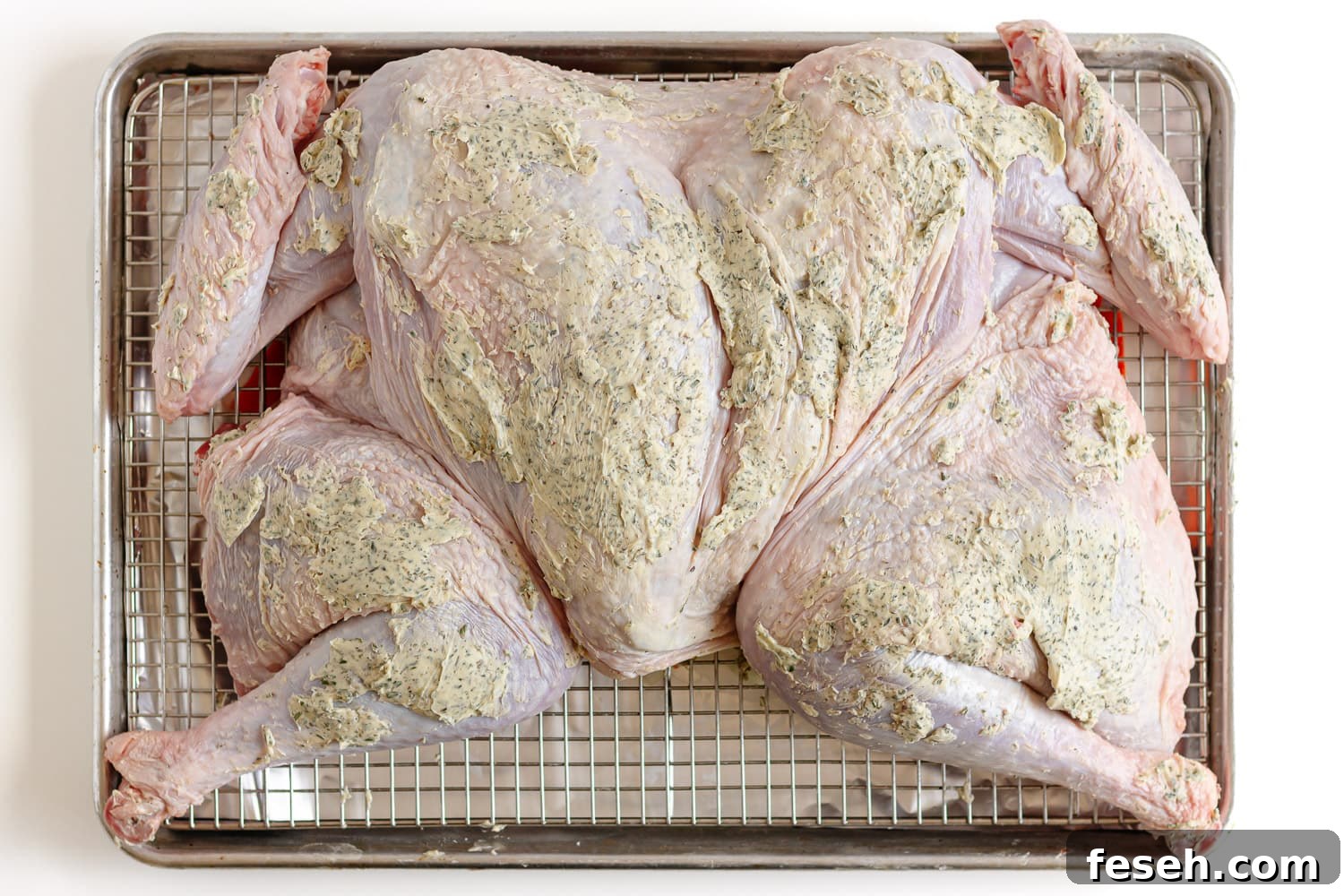 Herb butter slathered on a raw spatchcock turkey on a baking sheet.
