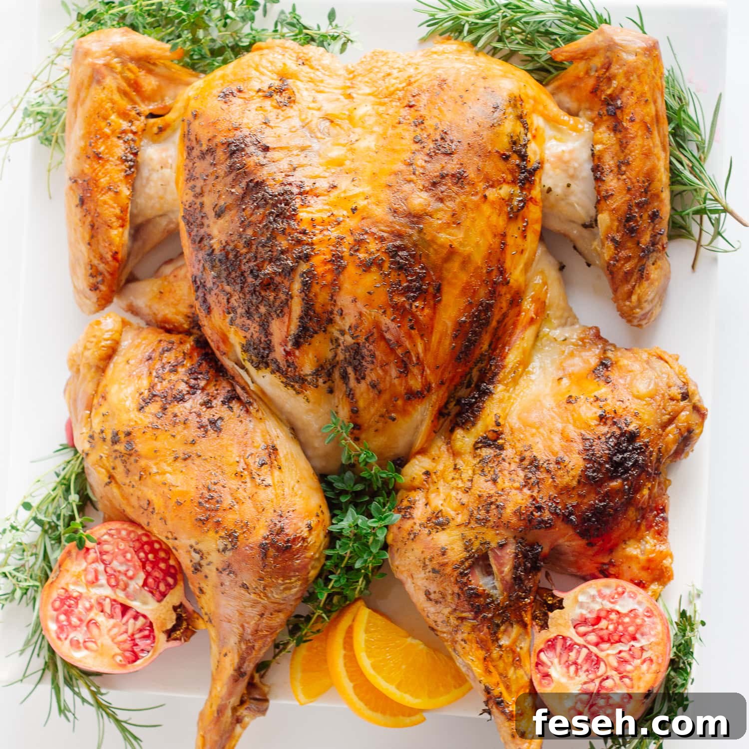 Roast spatchcock turkey on a serving platter garnished with herbs, pomegranate and orange slices.