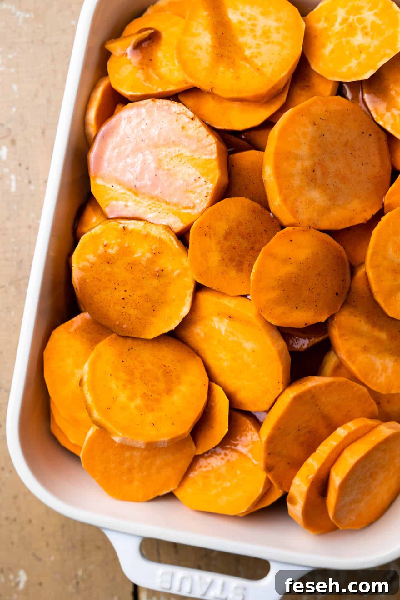 Brown sugar sauce poured over sliced sweet potato in a baking dish.